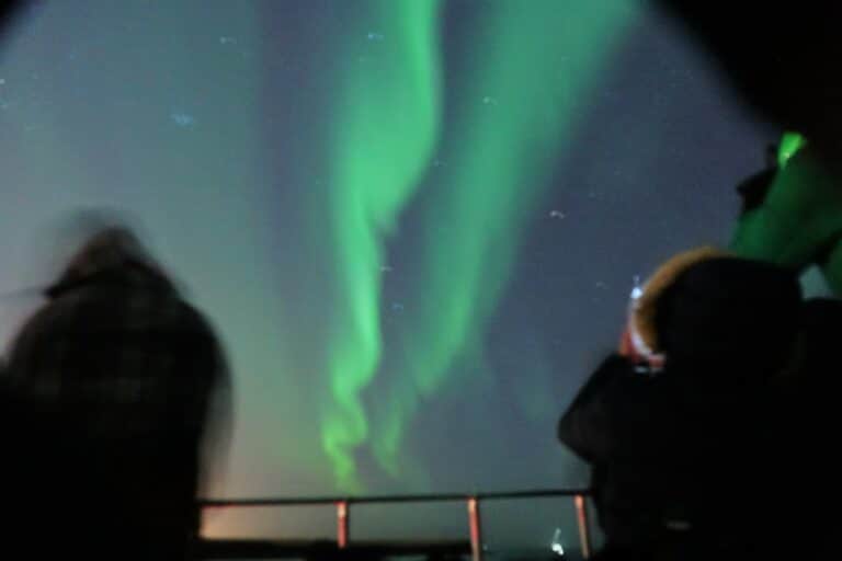 Image shows northern lights over Reykjavik, viewed from the deck of a luxury private yacht