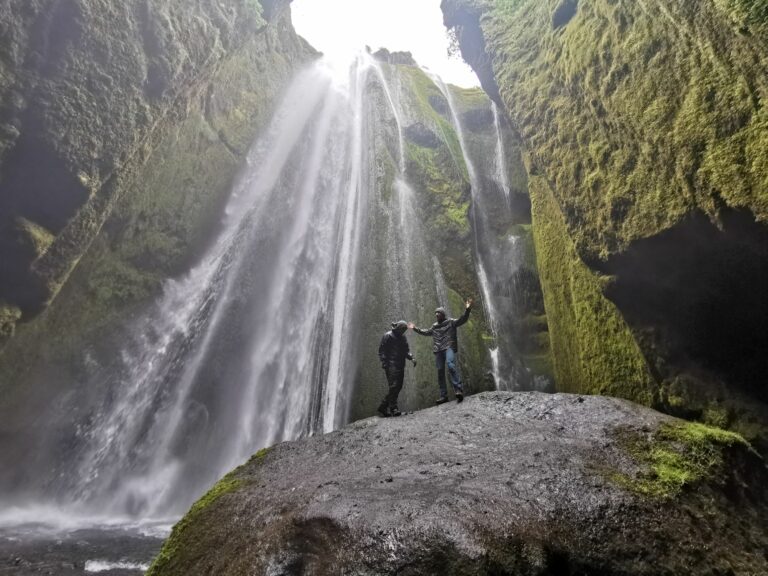 waterfalls reykjavikTwo people stand on a massive rock at the bottom of a waterfall in Iceland