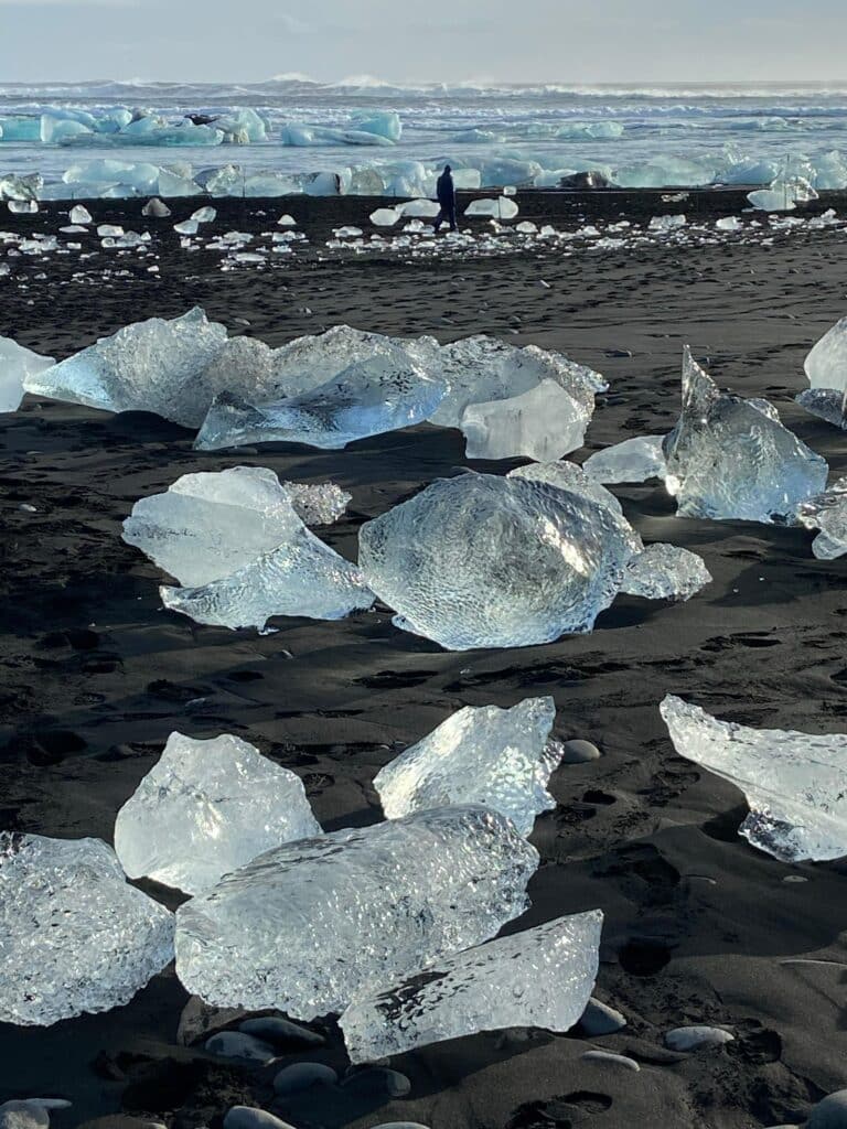 Photograph of diamond beach, a black sand beach in the south of iceland that is covered by large and small icebergs. The icebergs come from the nearby glacial face. The ice looks slightly blue. 